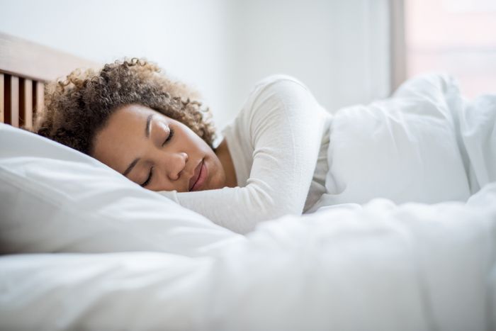 A woman sleeps with her head on a white pillow.